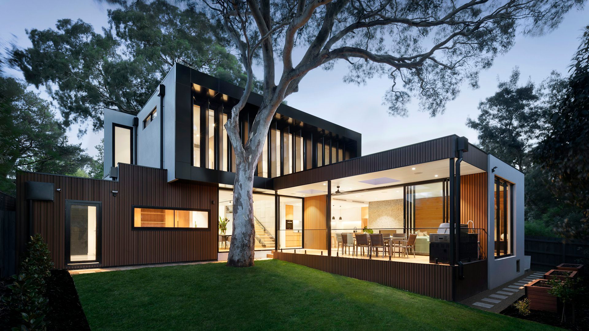 Two-storey house with timber cladding, seen from the lawn at dusk